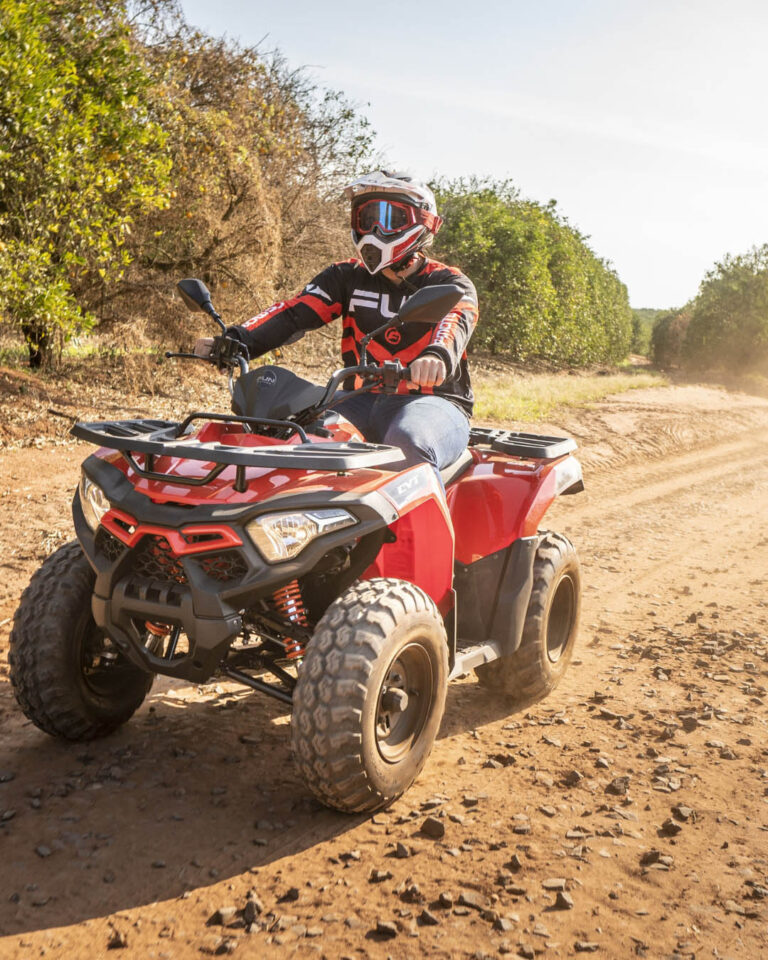A man riding an ATV along a rugged dirt road surrounded by trees and open terrain.